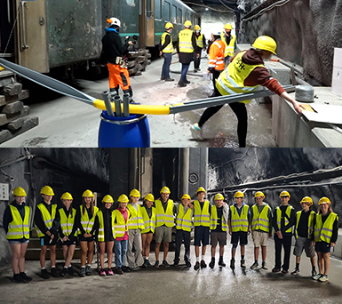Die Teilnehmer welche die grosse Murmelbahn im Stollen gebaut haben stehen stolz nach ihrem Teambuilding mit Warnvesten und Helm und posieren für ein Gruppenfoto